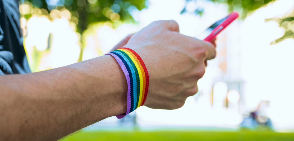 Imagem ilustrativa. Pessoa com uma pulseira com a bandeira LGBT tendo uma experiência positiva com a linguagem neutra em produto digital.