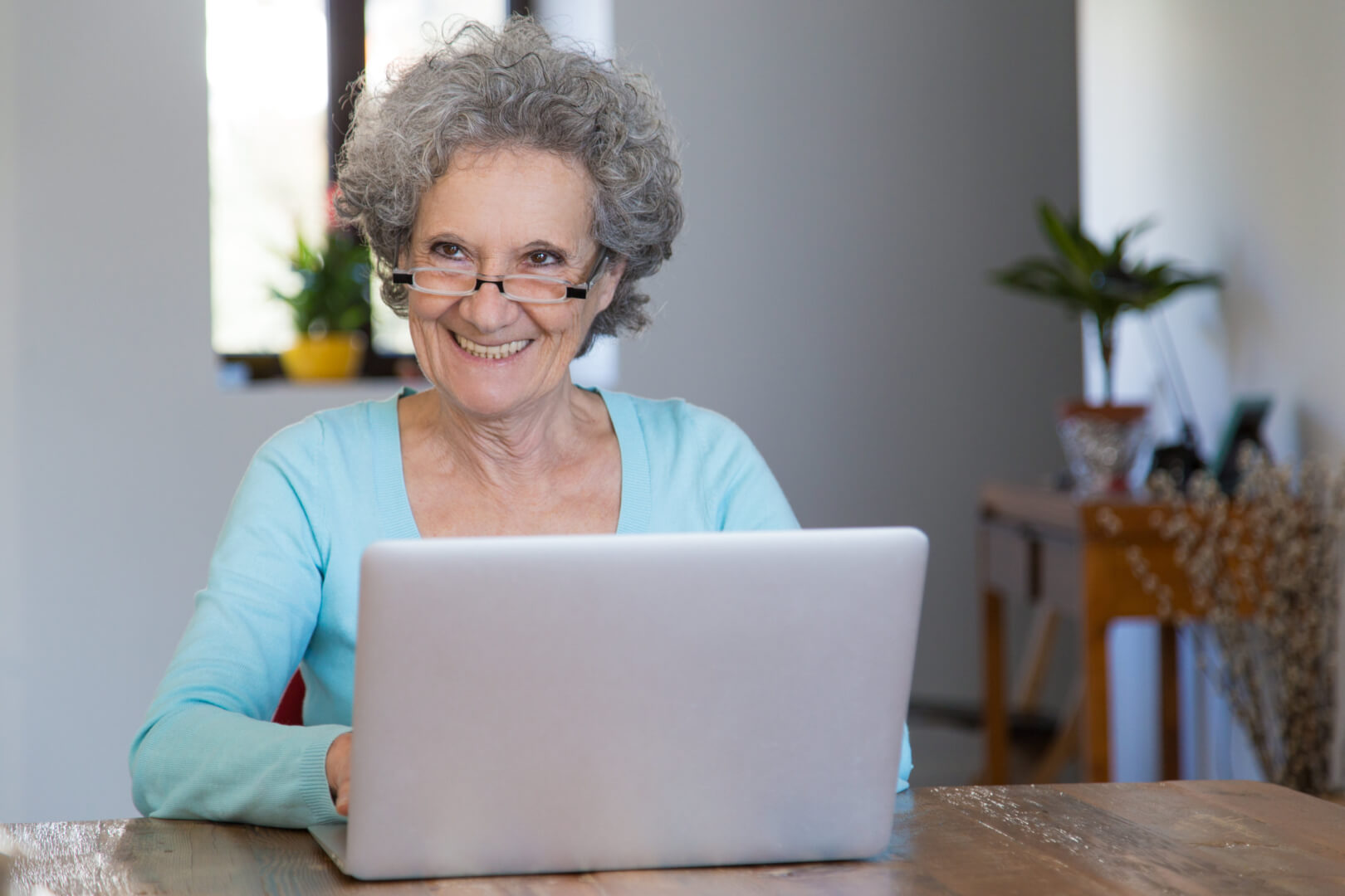 Mulher idosa sorrindo enquanto usa um laptop em um ambiente aconchegante. Representa a importância da acessibilidade e do design interativo para tornar a tecnologia mais intuitiva e inclusiva para todas as idades.
